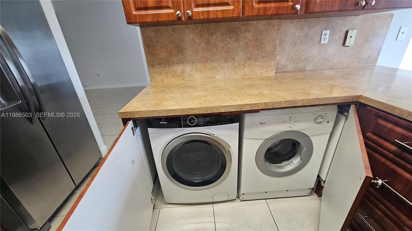 A kitchen with wood cabinets and a peninsula counter overlooks an adjacent tiled living area — 5800 SW 127th Ave # 2109, Miami FL 33183, MIAMI, FL