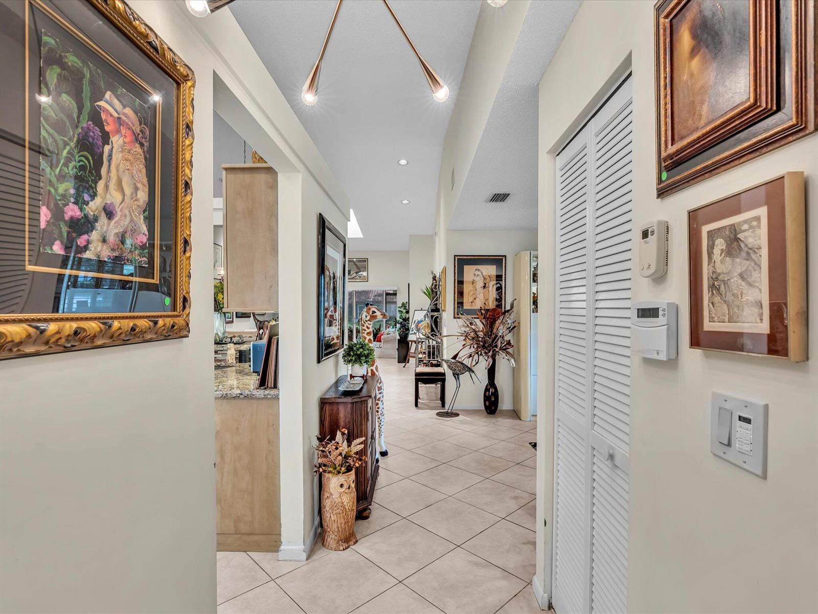 A tiled hallway leads past a kitchen and various artwork toward an open living area — 6454 Pointe Pleasant Circle, Delray Beach FL 33484, DELRAY BEACH, FL