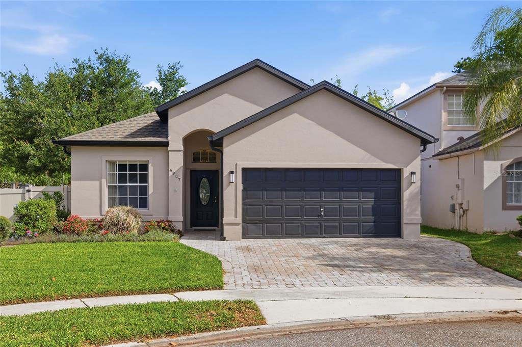 A single-story house with a beige stucco exterior, dark garage door, and a paver driveway — 4907 OLDE KERRY DRIVE, ORLANDO, FL