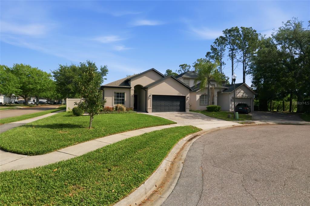 A beige single-story house with a dark garage and a paved driveway sits on a corner — 4907 OLDE KERRY DRIVE, ORLANDO, FL