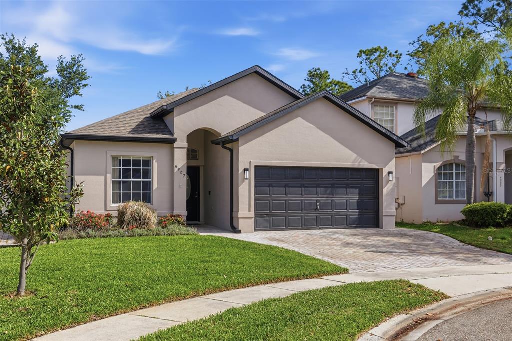 A single-story house with a tan stucco exterior, a dark garage door, and a paved driveway — 4907 OLDE KERRY DRIVE, ORLANDO, FL
