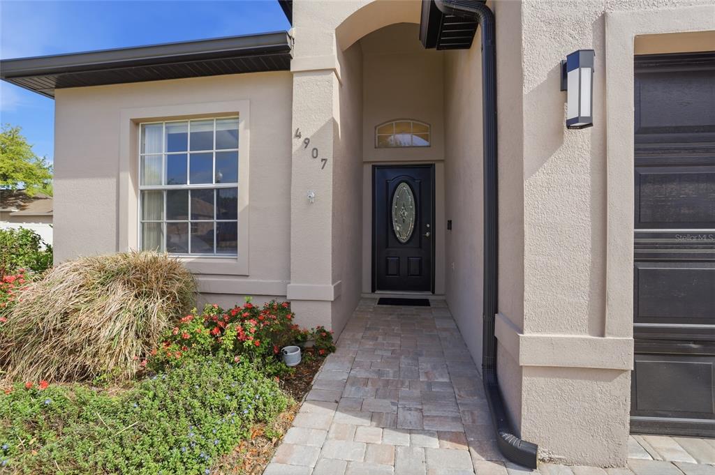 The exterior view shows a tan stucco house entrance with a paved walkway and door — 4907 OLDE KERRY DRIVE, ORLANDO, FL