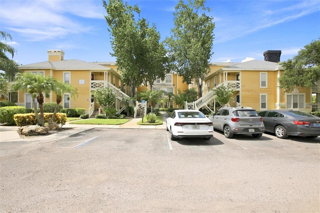 A yellow apartment building exterior with a parking lot and several cars in front — 115 112TH AVENUE NE UNIT 307, ST PETERSBURG, FL