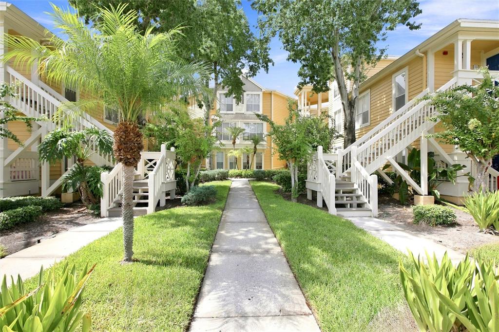 A sidewalk leads between two yellow apartment buildings with white exterior staircases and palm trees — 115 112TH AVENUE NE UNIT 307, ST PETERSBURG, FL