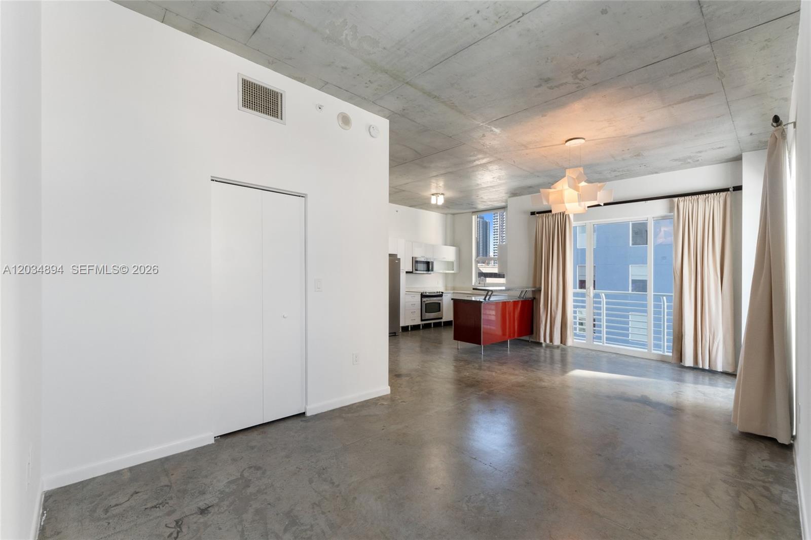 An open-concept living area features concrete floors, a raw concrete ceiling, and a red kitchen island — 133 NE 2nd Ave # 801, Miami FL 33132, MIAMI, FL