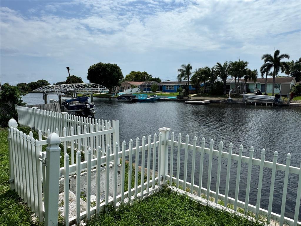 A white vinyl fence borders a canal with several docked boats and waterfront houses — 1345 BASSWOOD DRIVE, HOLIDAY, FL