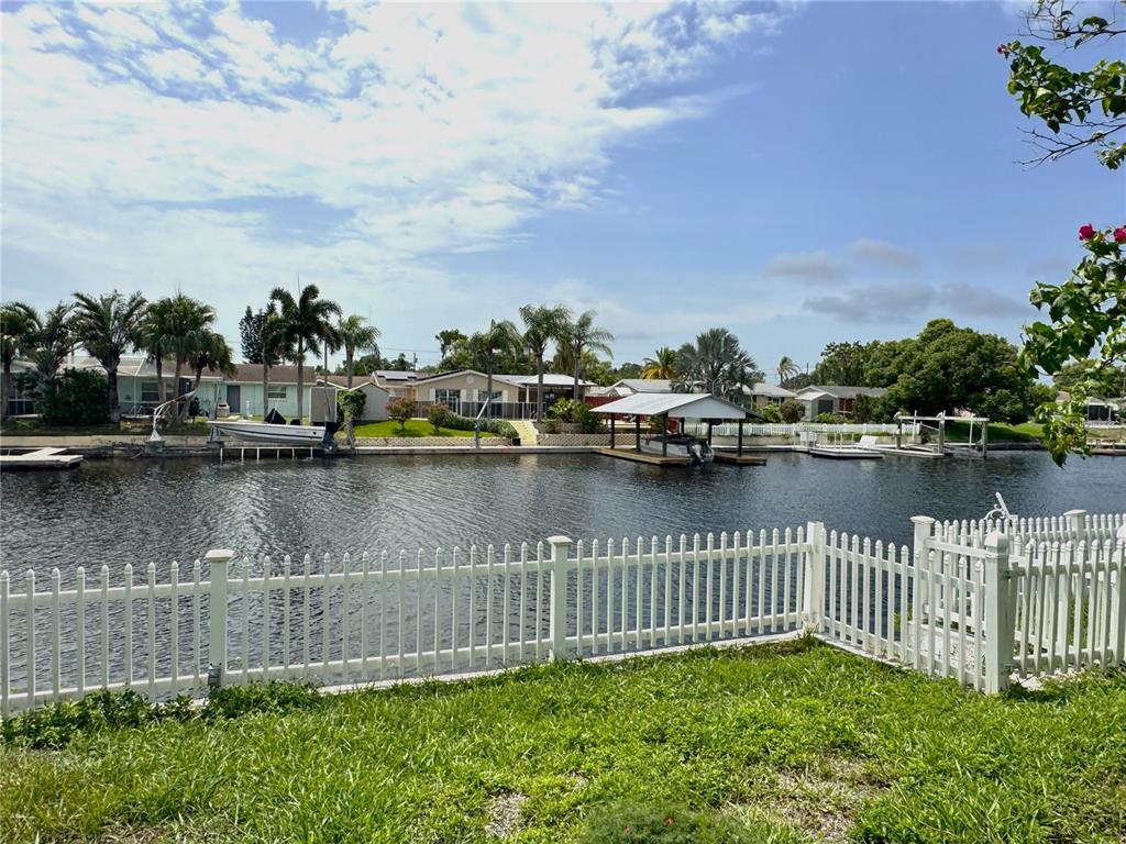 A white picket fence overlooks a canal with boat docks and houses in the background — 1345 BASSWOOD DRIVE, HOLIDAY, FL