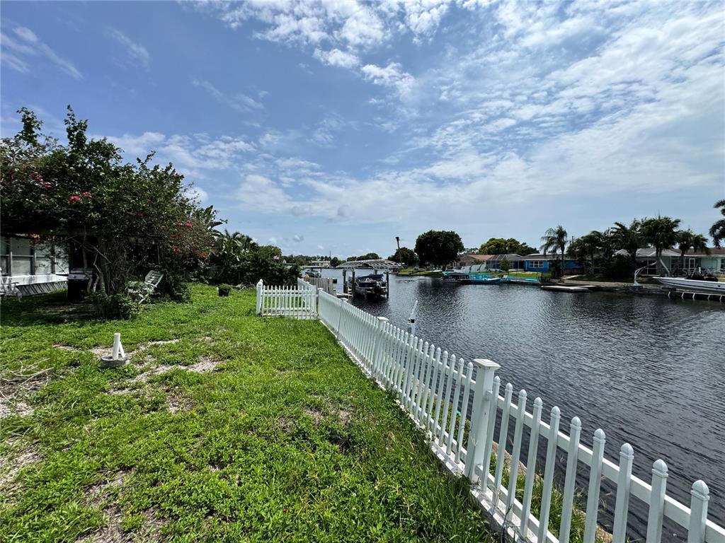 A white vinyl fence borders a grassy yard alongside a canal with boat docks — 1345 BASSWOOD DRIVE, HOLIDAY, FL