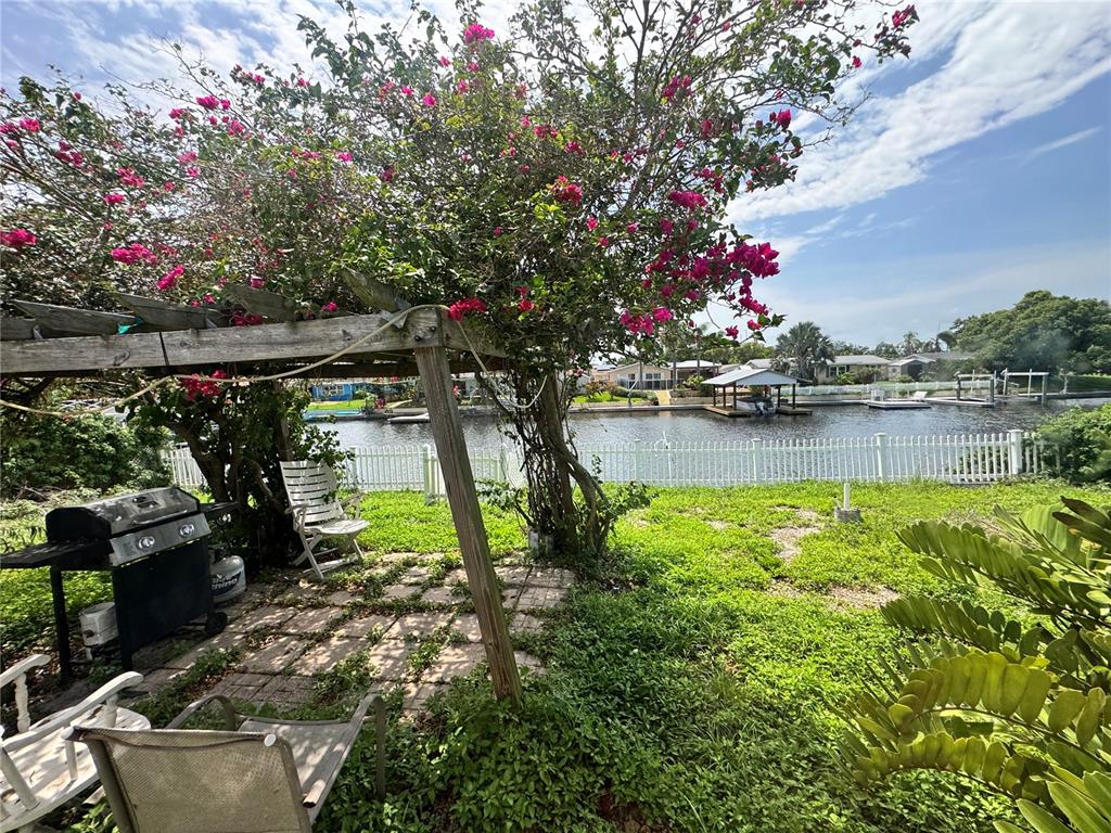 A backyard patio features a wooden pergola covered in bougainvillea overlooking a canal with docks — 1345 BASSWOOD DRIVE, HOLIDAY, FL
