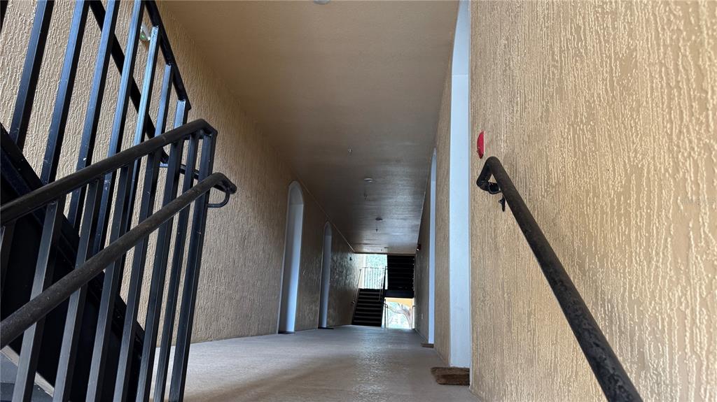 An outdoor apartment building corridor features a concrete walkway, metal railings, and a staircase — 3224 DANTE DRIVE UNIT 207, ORLANDO, FL