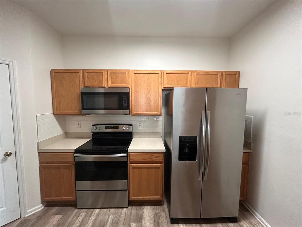 A kitchen features wood cabinets, stainless steel appliances, and light-colored countertops — 3224 DANTE DRIVE UNIT 207, ORLANDO, FL