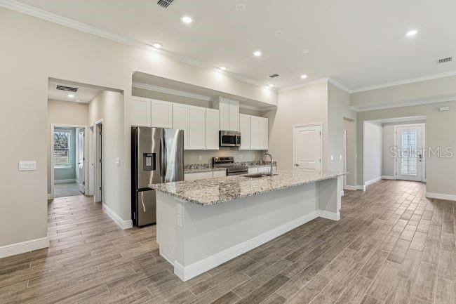 A kitchen features white cabinets, granite countertops, a stainless steel refrigerator, and wood-look tile flooring — 4360 WINESAP WAY, LAKELAND, FL