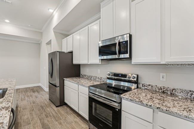 A kitchen features white cabinets, granite countertops, stainless steel appliances, and wood-look tile flooring — 4360 WINESAP WAY, LAKELAND, FL