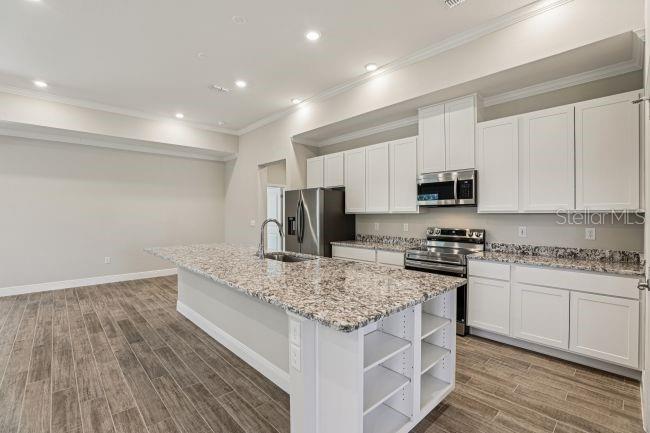 A modern kitchen features white cabinets, granite countertops, stainless steel appliances, and wood-look tile flooring — 4360 WINESAP WAY, LAKELAND, FL