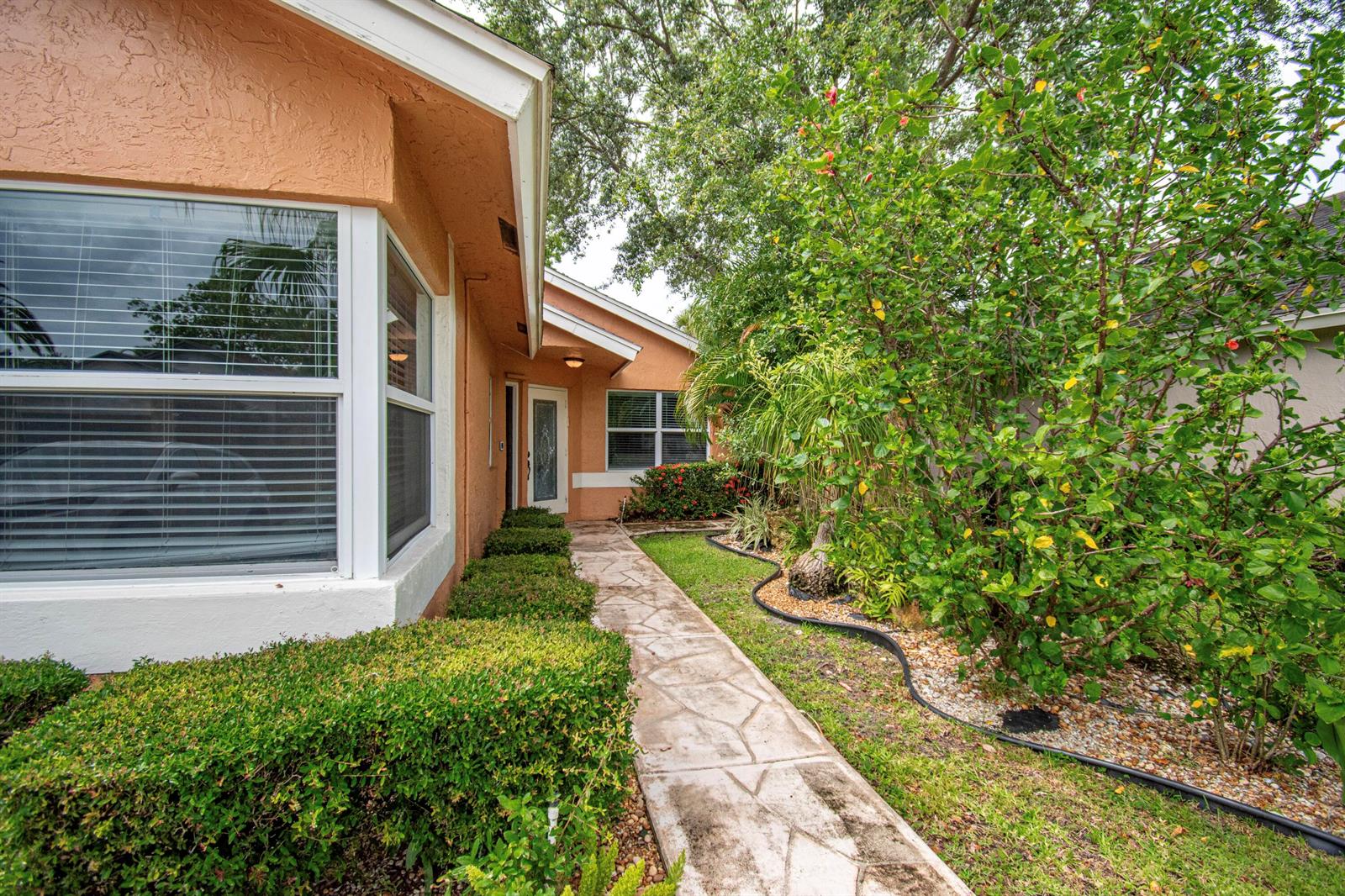 A stone walkway leads to the front entrance of a peach-colored house with landscaping — 7601 Martinique Boulevard, Boca Raton FL 33433, BOCA RATON, FL