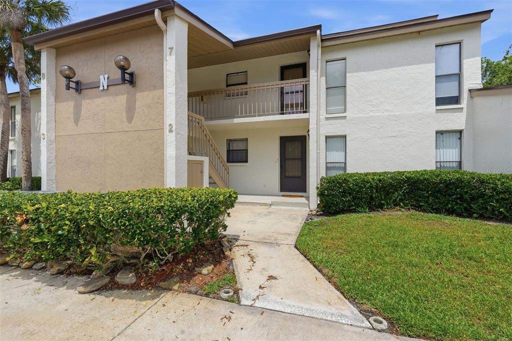 A two-story apartment building exterior features a concrete walkway, stairs, and a second-floor balcony — 1200 TARPON WOODS BOULEVARD UNIT N2, PALM HARBOR, FL