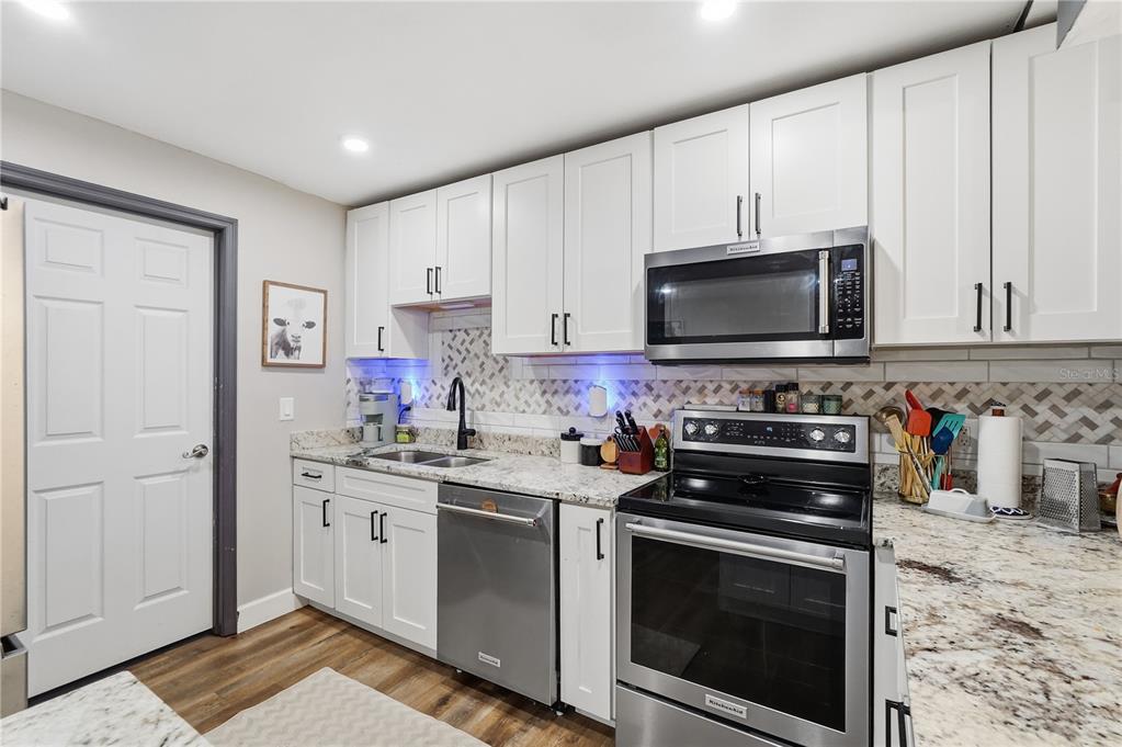 A kitchen features white cabinets, stainless steel appliances, granite countertops, and a patterned tile backsplash — 1200 TARPON WOODS BOULEVARD UNIT N2, PALM HARBOR, FL