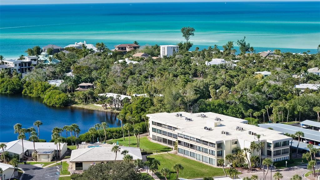 An aerial view shows a multi-story apartment building near a lake and the ocean — 199 WHISPERING SANDS DRIVE UNIT 204, SARASOTA, FL