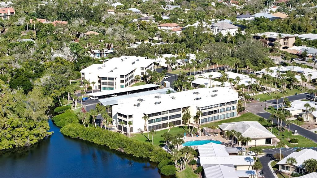 An aerial view shows two multi-story apartment buildings with white roofs near a small lake — 199 WHISPERING SANDS DRIVE UNIT 204, SARASOTA, FL