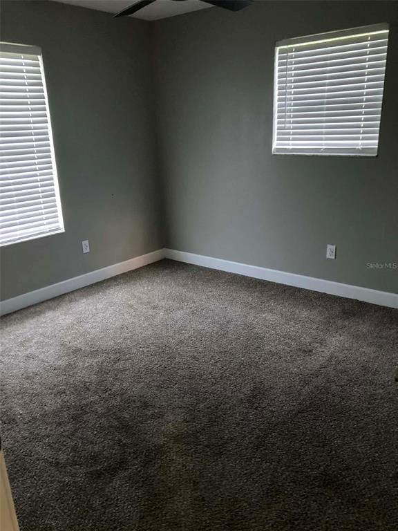 An empty bedroom features gray walls, dark carpeting, white trim, and two windows with blinds — 1135 SIBONEY STREET NW, PALM BAY, FL