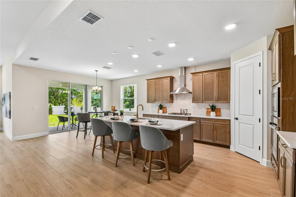 A modern kitchen features wood cabinets, a white quartz island, and gray bar stools — 3326 WOLF LAKE AVENUE, APOPKA, FL