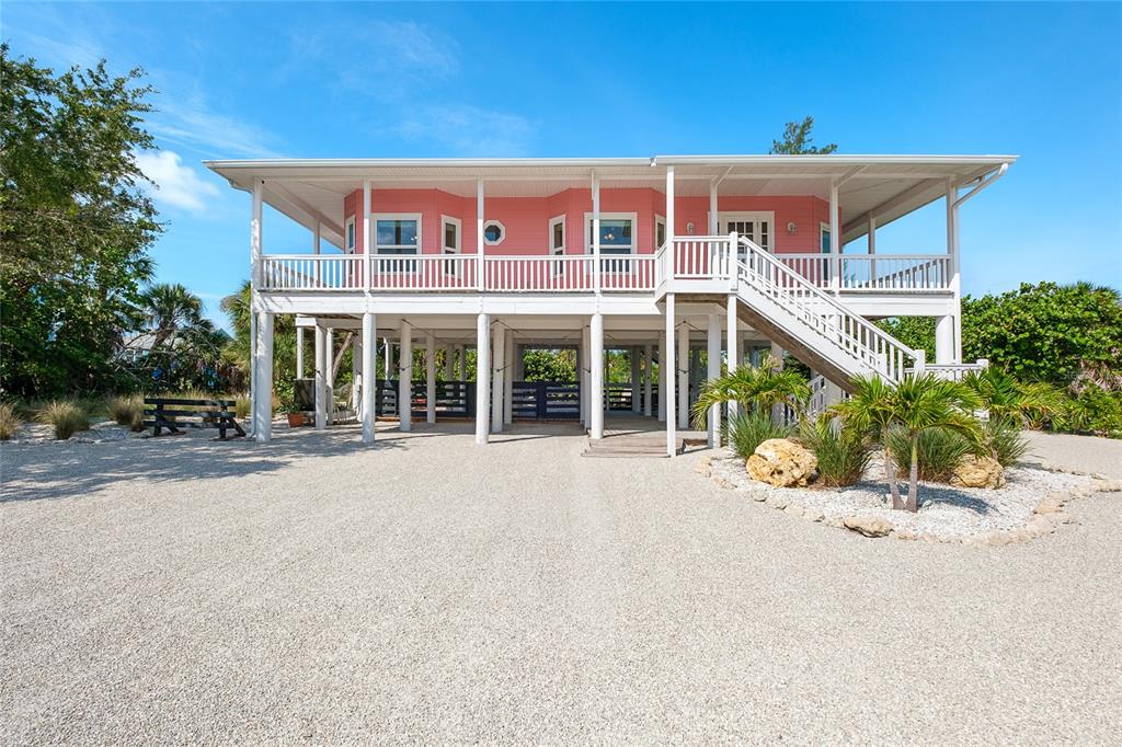 A pink stilt house with a wraparound porch stands above a gravel driveway — 141 GASPARILLA WAY, PLACIDA, FL