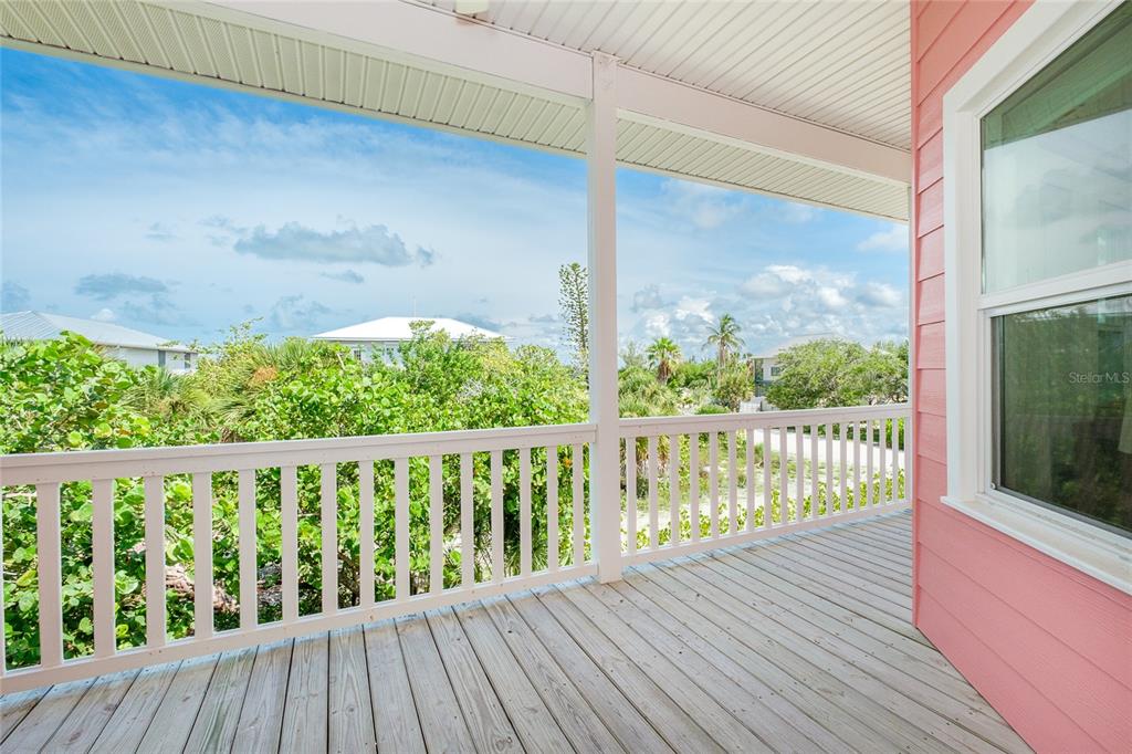 A covered wooden balcony features white railings and a view of surrounding trees and houses — 141 GASPARILLA WAY, PLACIDA, FL