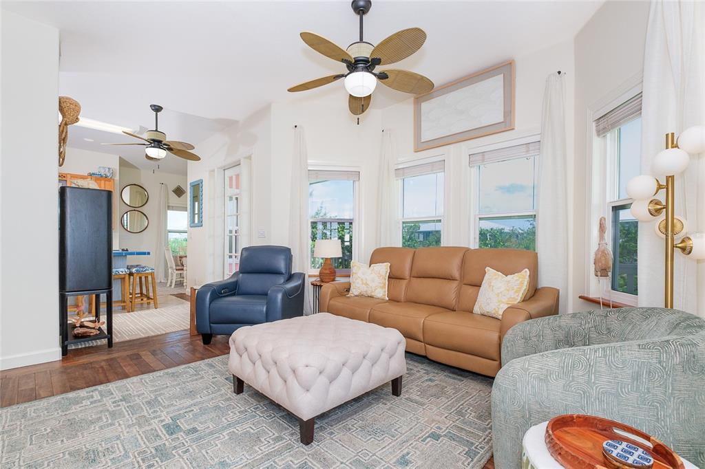 A living room features a brown leather sofa, blue armchair, tufted ottoman, and ceiling fans — 141 GASPARILLA WAY, PLACIDA, FL