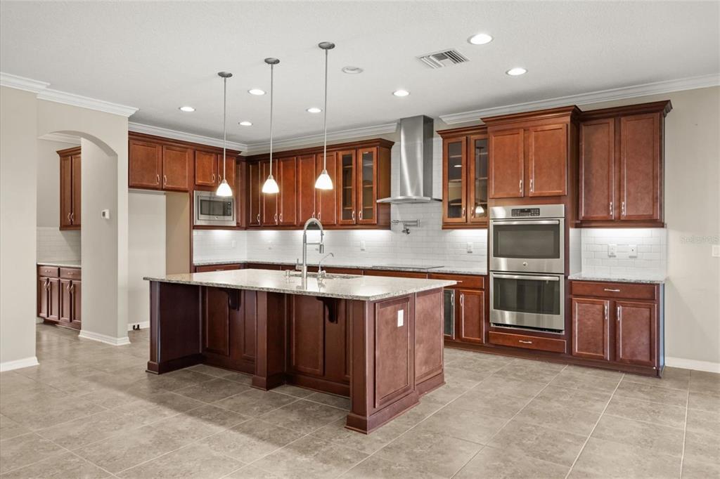 A kitchen with dark wood cabinets, a large granite island, and stainless steel appliances — 1831 VIA LAGO DRIVE, LAKELAND, FL