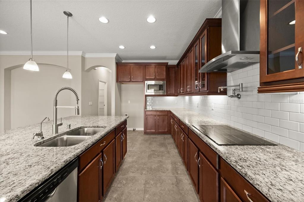 A kitchen features dark wood cabinets, granite countertops, a stainless steel range, and a central island — 1831 VIA LAGO DRIVE, LAKELAND, FL