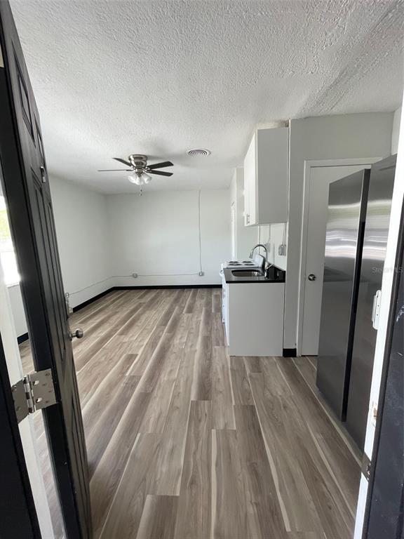 A room with light wood-look flooring, a ceiling fan, and a small kitchen area — 707 ROSERY ROAD NW UNIT 3, LARGO, FL