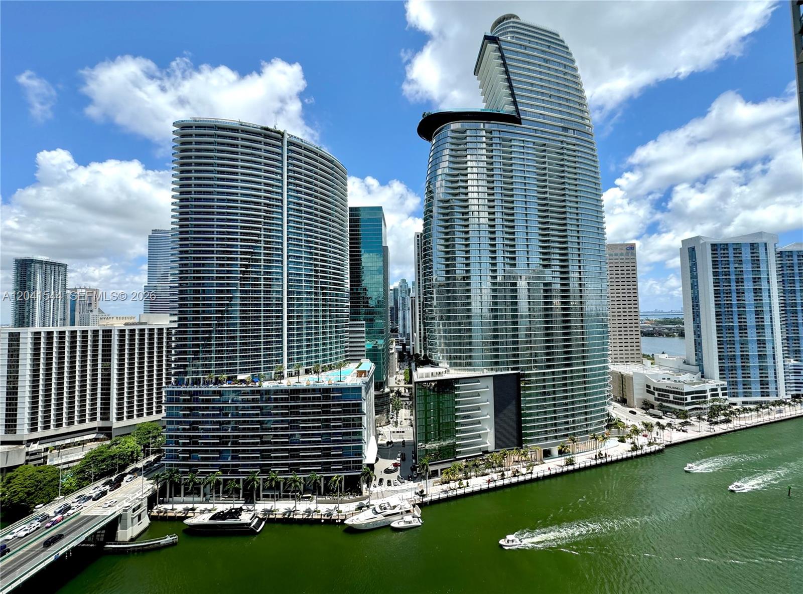 An exterior view shows two tall glass skyscrapers along a river with boats — 475 Brickell Ave # 2512, Miami FL 33131, MIAMI, FL