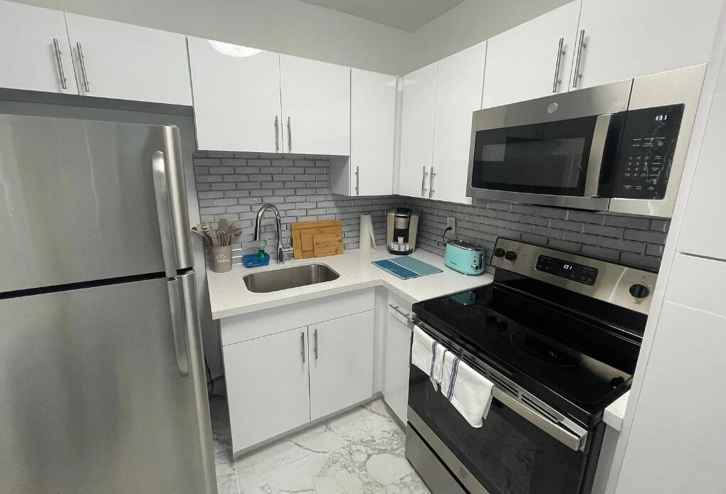 A small kitchen features white cabinets, stainless steel appliances, a gray subway tile backsplash, and marble-patterned flooring — 201 S Ocean Boulevard # 7, Boca Raton FL 33432, BOCA RATON, FL