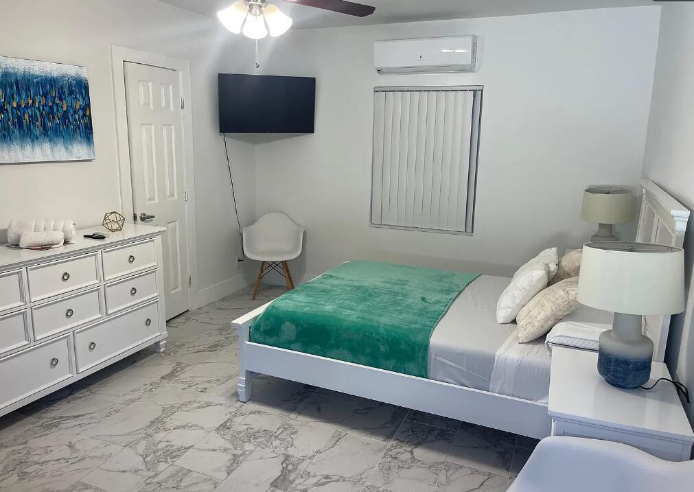 A bedroom with a white bed, dresser, marble-look tile flooring, and a wall-mounted television — 201 S Ocean Boulevard # 7, Boca Raton FL 33432, BOCA RATON, FL