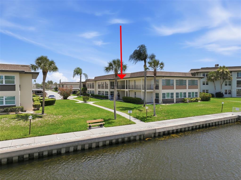 An exterior view of a multi-story apartment building situated along a canal with landscaping — 5108 AMULET DRIVE UNIT 205, NEW PORT RICHEY, FL