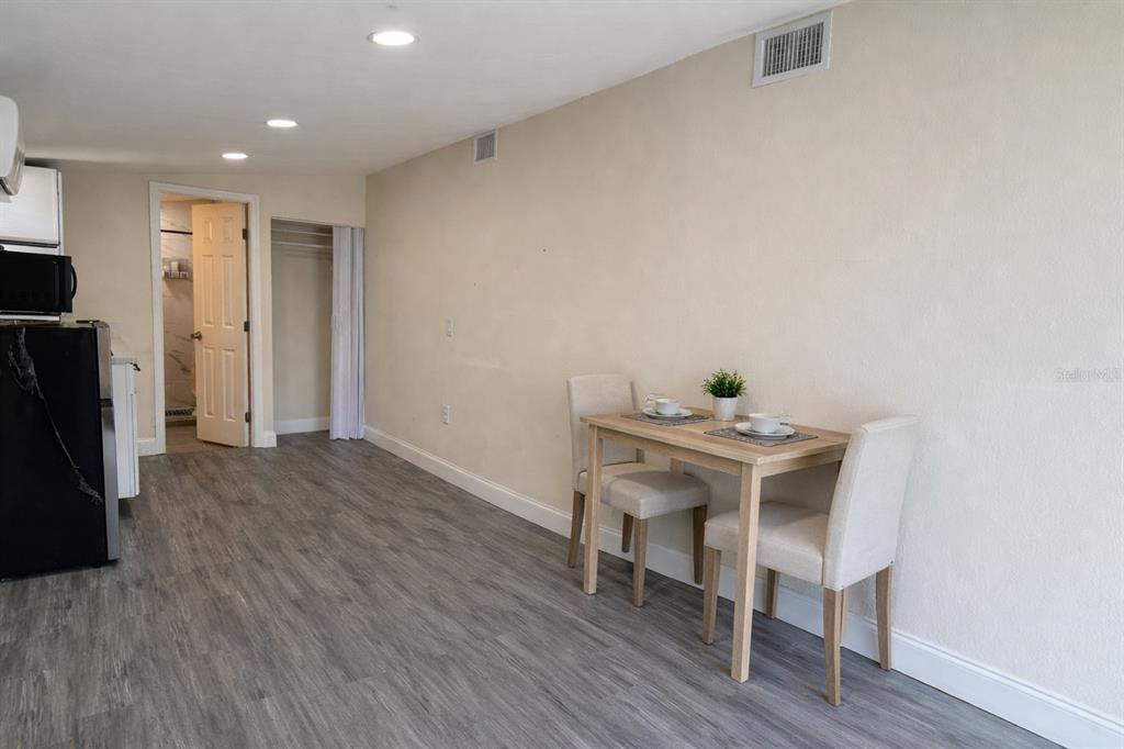 A small dining area with a wooden table and two chairs sits against a beige wall — 5620 1ST STREET UNIT rear, ZEPHYRHILLS, FL
