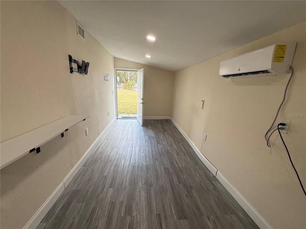 A room with light-colored walls, wood-look flooring, a wall-mounted air conditioner, and an open door — 5620 1ST STREET UNIT rear, ZEPHYRHILLS, FL