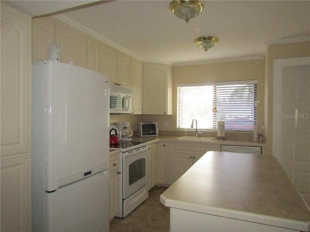 A kitchen features white cabinets, white appliances, a central island, and a window with blinds — 1211 SAXONY CIRCLE UNIT A-1, PUNTA GORDA, FL
