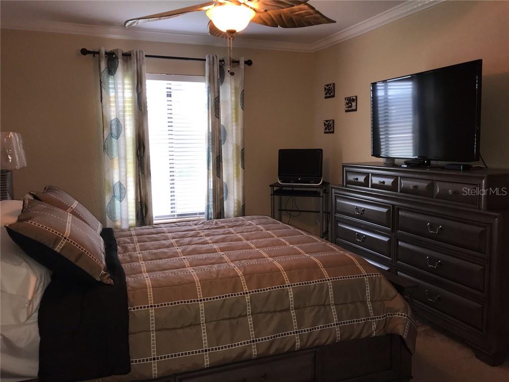 A bedroom features a bed with brown bedding, a dresser with a television, and window curtains — 1211 SAXONY CIRCLE UNIT A-1, PUNTA GORDA, FL