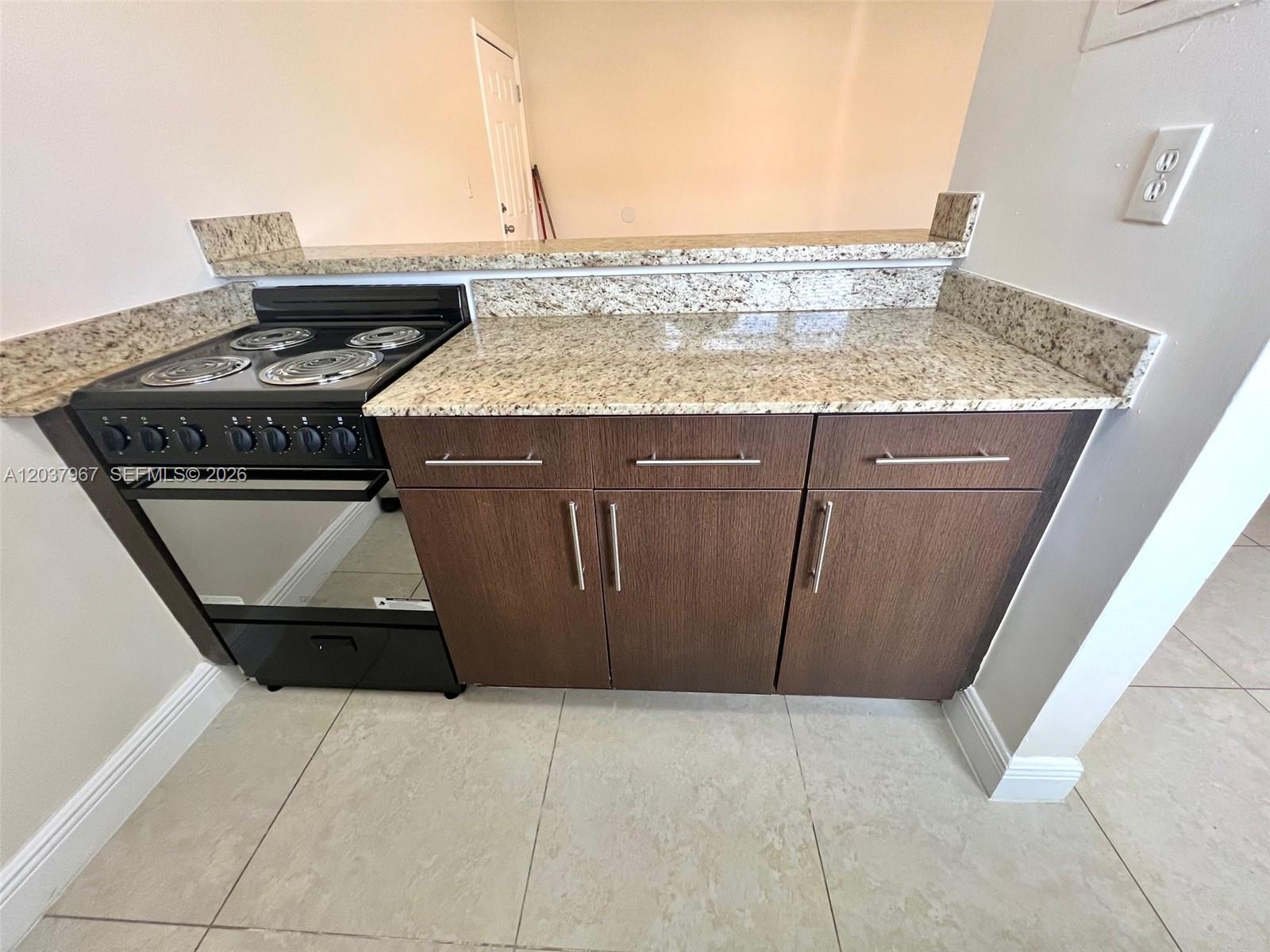 A kitchen features a black electric stove, granite countertops, and dark wood cabinets — 685 NE 85th St # 9, Miami FL 33138, MIAMI, FL