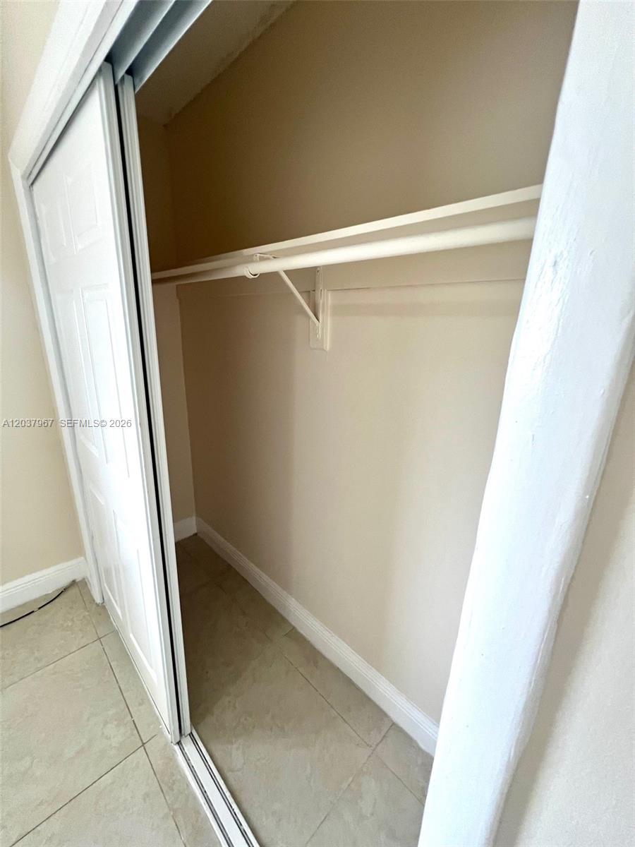 A closet with white sliding doors, a shelf, and a hanging rod over tiled floors — 685 NE 85th St # 9, Miami FL 33138, MIAMI, FL