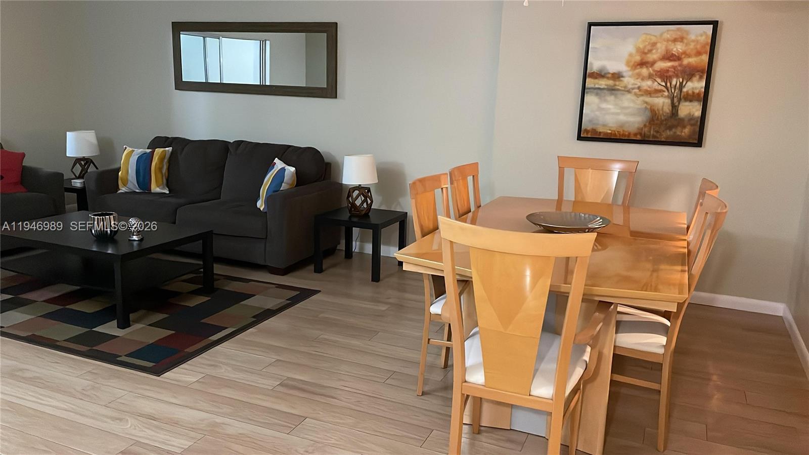 A living and dining area features a grey sofa, wooden table, and light wood flooring — 121 SE 3rd Ave # 201, Dania Beach FL 33004, DANIA BEACH, FL