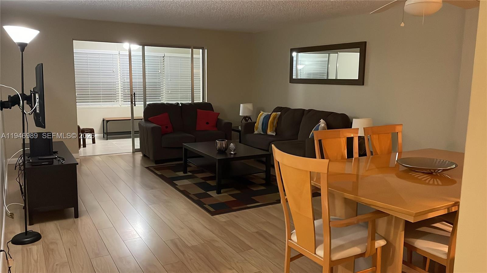 A living and dining area features wood-look flooring, dark furniture, and a sliding glass door — 121 SE 3rd Ave # 201, Dania Beach FL 33004, DANIA BEACH, FL