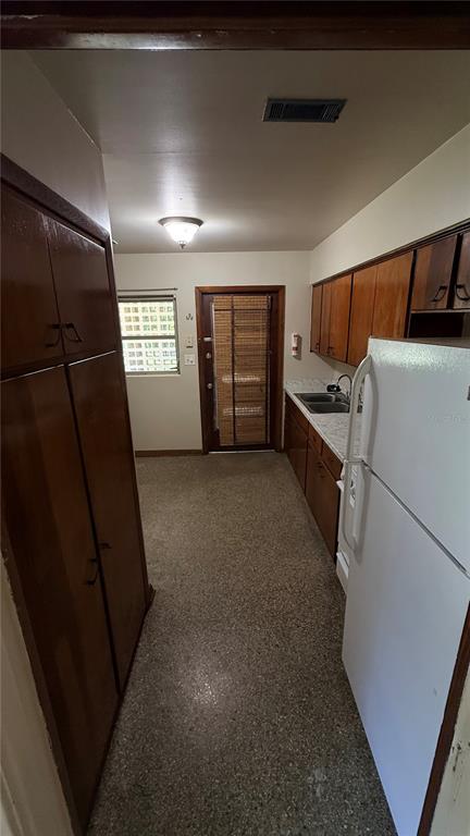 A galley kitchen features wood cabinets, a white refrigerator, and a speckled floor — 932 NE 6TH AVENUE, GAINESVILLE, FL