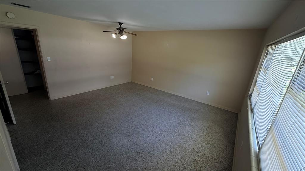 An empty room with beige walls, gray carpet, a ceiling fan, and large window blinds — 932 NE 6TH AVENUE, GAINESVILLE, FL