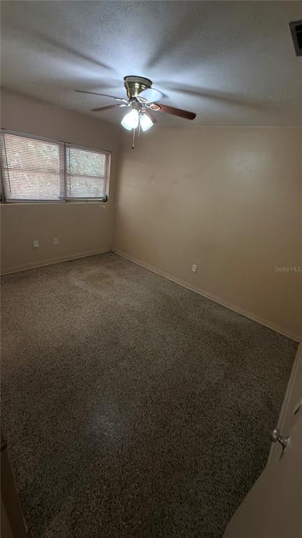 An empty bedroom with beige walls, a ceiling fan, and speckled carpet flooring — 932 NE 6TH AVENUE, GAINESVILLE, FL