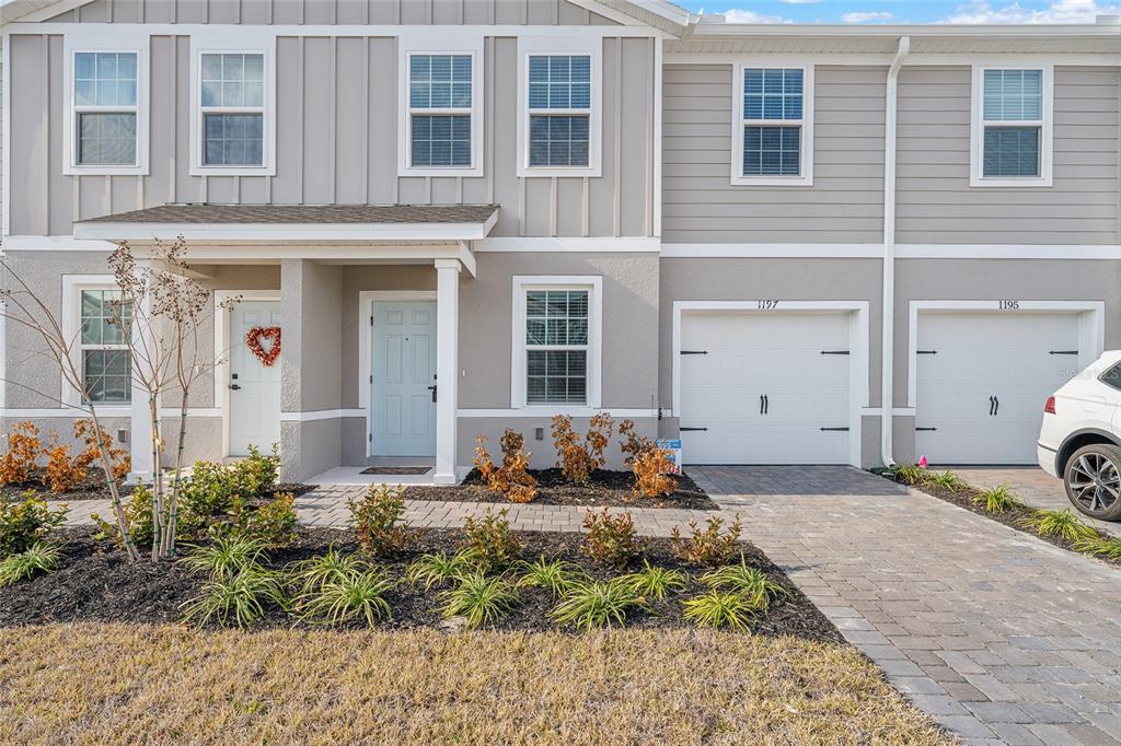 A two-story townhouse exterior features light gray siding, a paved driveway, and a small front garden — 1197 PORT BLUE WAY, LADY LAKE, FL