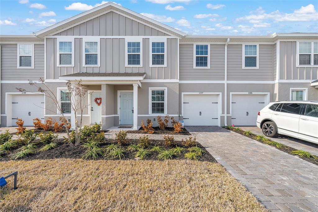 A row of light gray townhouses with white garage doors and a paved driveway — 1197 PORT BLUE WAY, LADY LAKE, FL