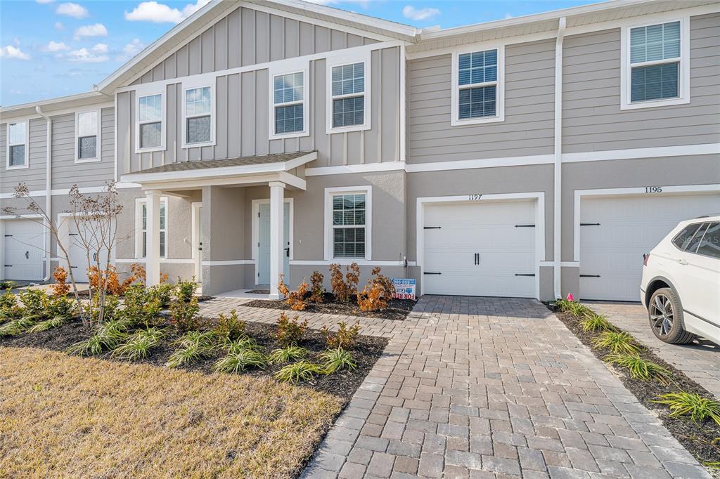 A two-story townhouse exterior features a paved driveway, a white garage door, and landscaping — 1197 PORT BLUE WAY, LADY LAKE, FL