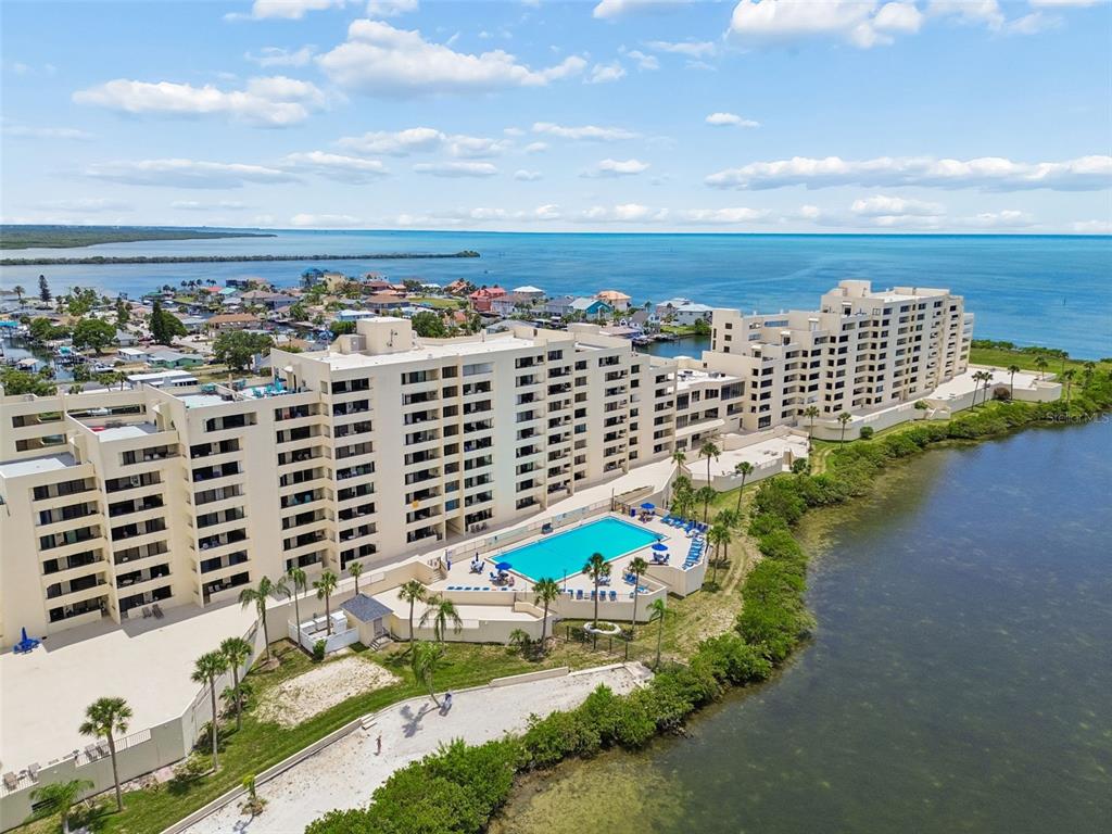 An aerial view shows a large waterfront apartment complex with a pool and palm trees — 5915 SEA RANCH DRIVE UNIT 611, HUDSON, FL
